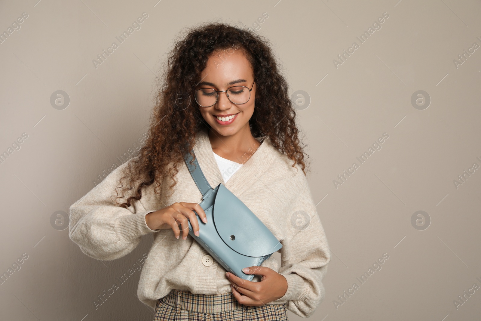 Photo of Beautiful African American woman with stylish waist bag on beige background