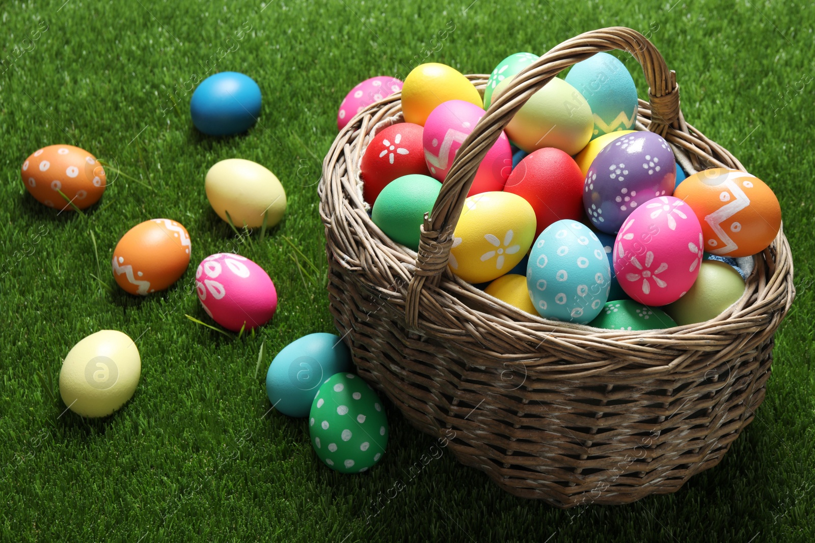 Photo of Colorful Easter eggs in basket on green grass