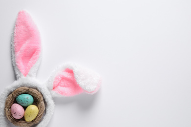 Headband with bunny ears and painted eggs on white background, top view. Easter holiday