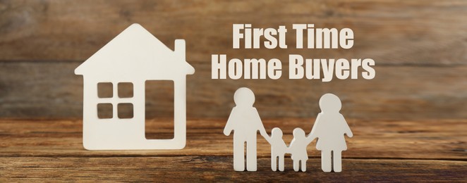 First time home buyers. Figures of family and house on wooden table. Banner design