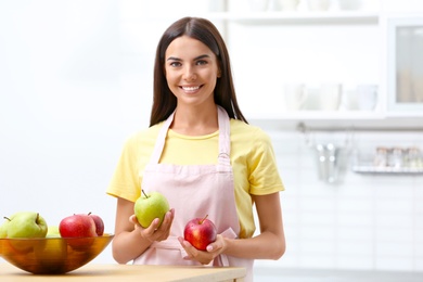 Happy woman holding fresh apples in kitchen