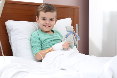 Photo of Little child with intravenous drip and toy in hospital bed