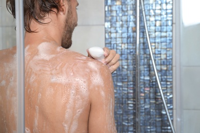 Photo of Attractive young man taking shower with soap in bathroom. Space for text