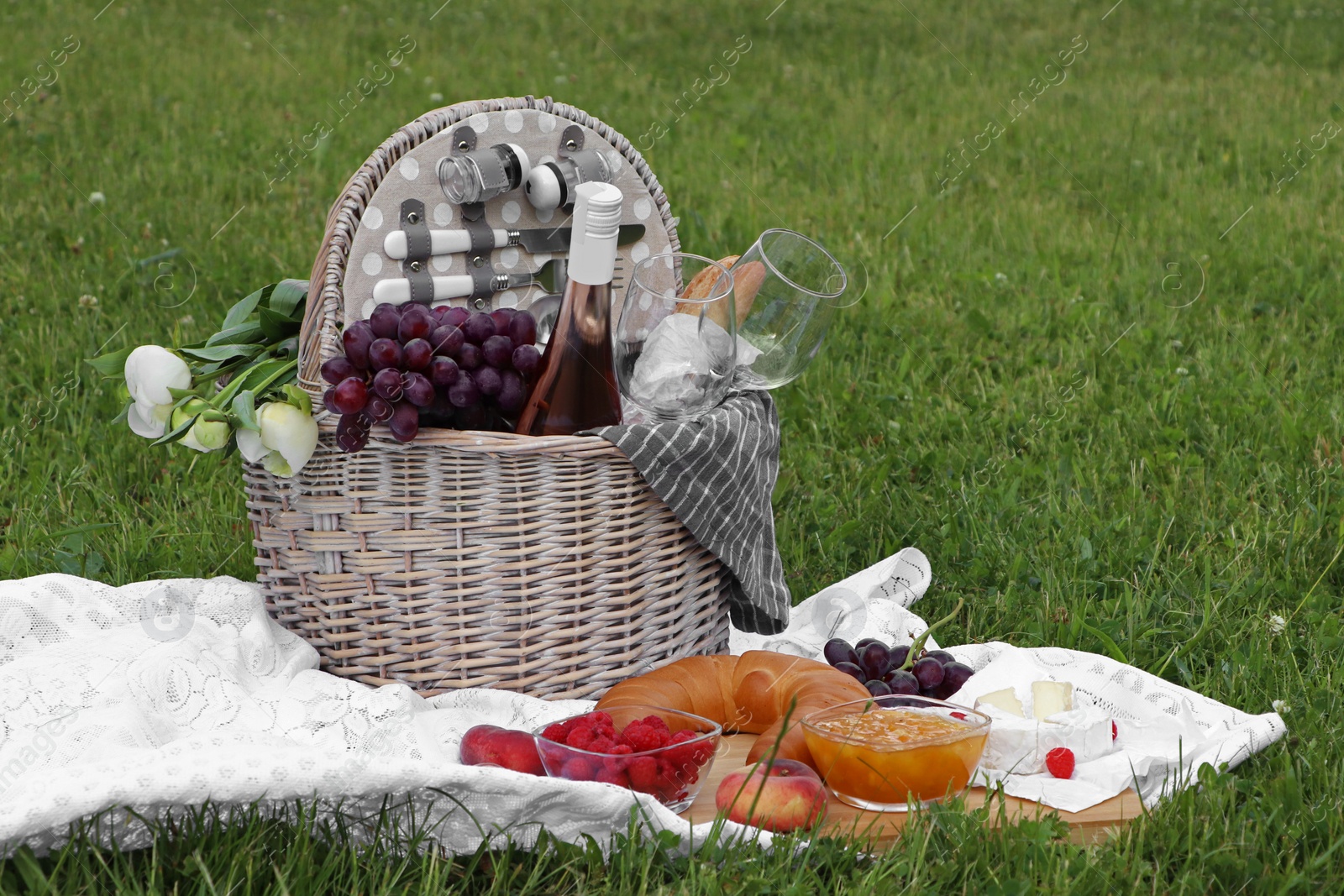 Photo of Picnic blanket with tasty food, flowers, basket and cider on green grass outdoors