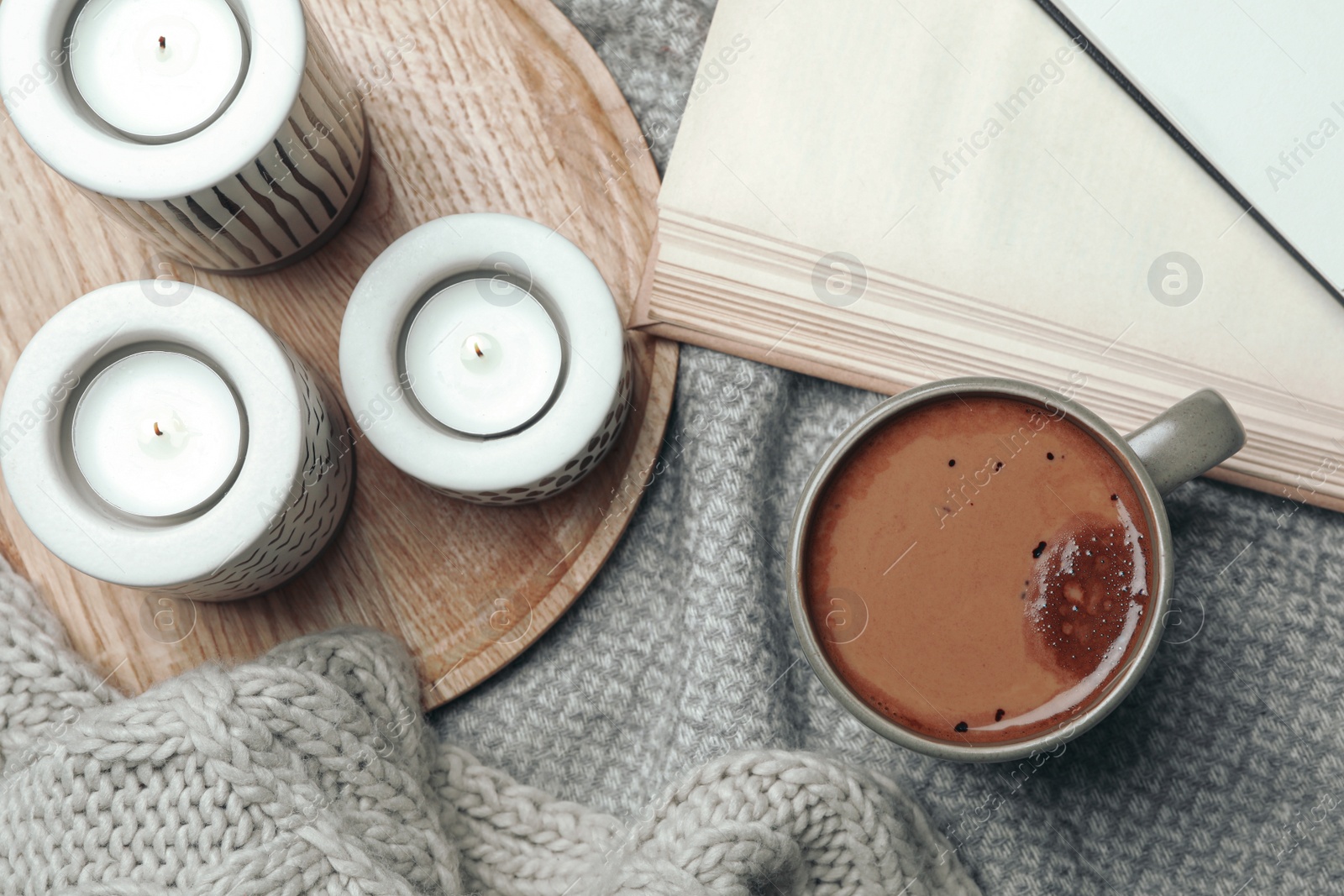 Photo of Cup of delicious hot winter drink and candles on grey fabric, flat lay. Winter drink