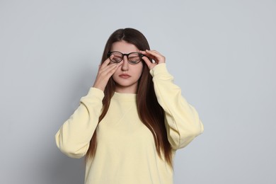 Young woman suffering from eyestrain on light background