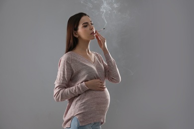 Photo of Young pregnant woman smoking cigarette on grey background