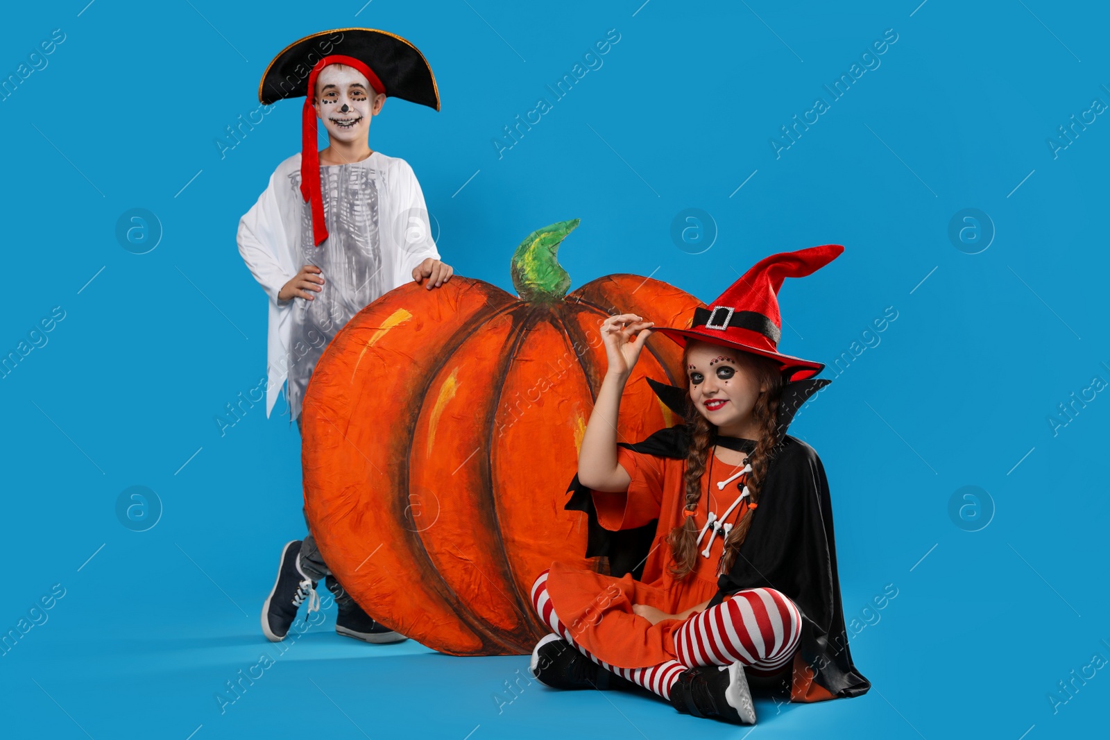 Photo of Cute little kids with decorative pumpkin wearing Halloween costumes on light blue background