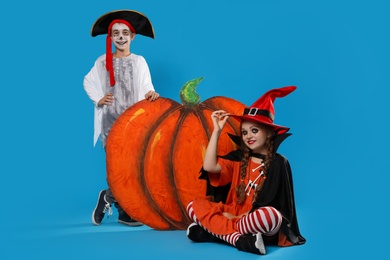 Photo of Cute little kids with decorative pumpkin wearing Halloween costumes on light blue background