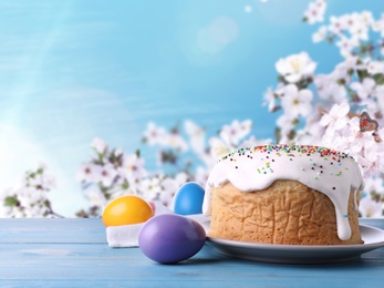 Image of Easter cake and dyed eggs on blue wooden table outdoors, space for text