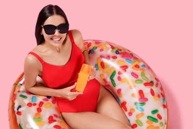 Photo of Young woman with sun protection cream on inflatable ring against pink background, above view