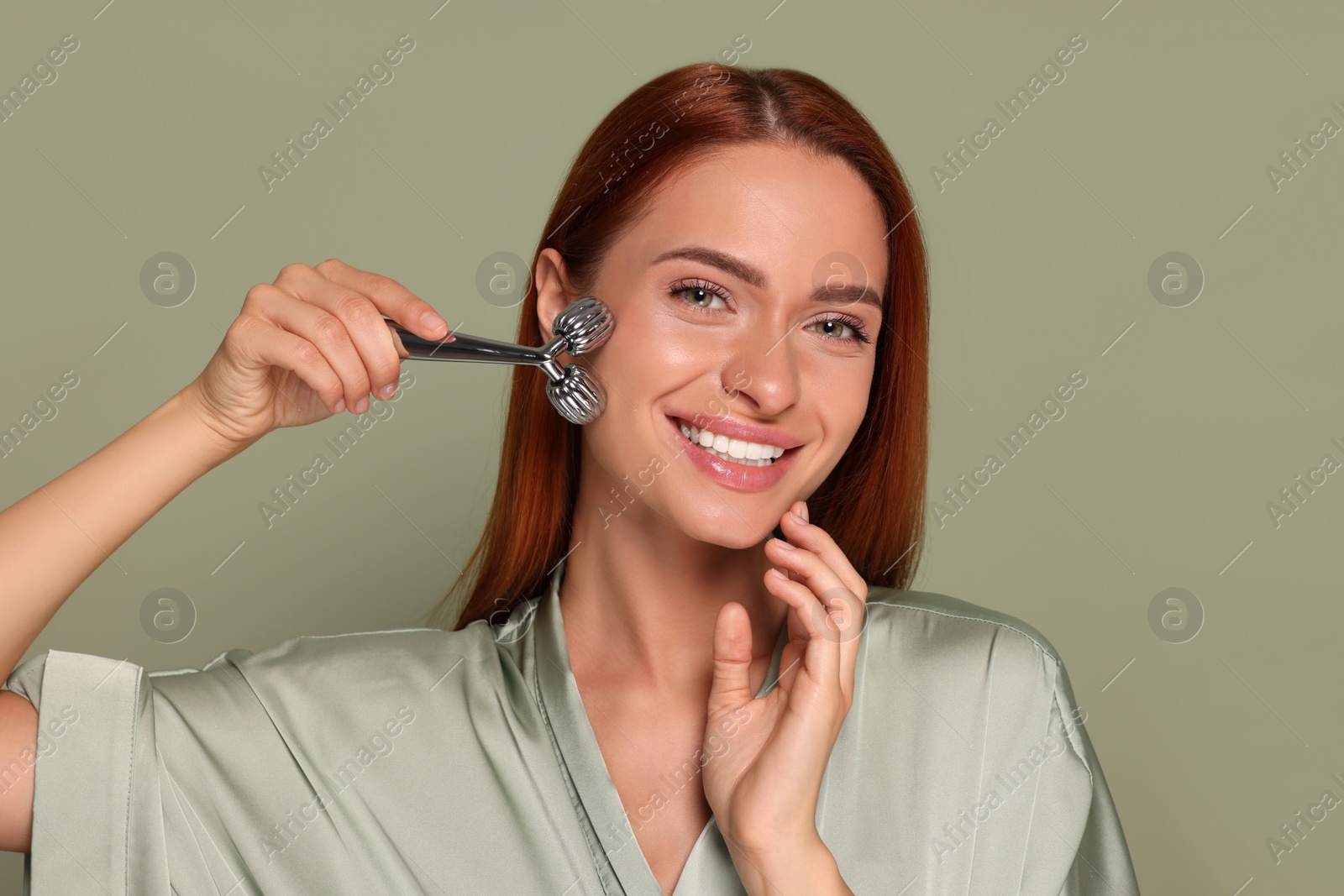 Photo of Young woman massaging her face with metal roller on green background