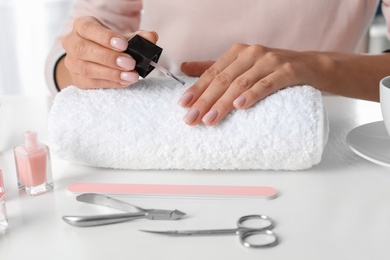 Woman applying nail polish at table, closeup. At-home manicure