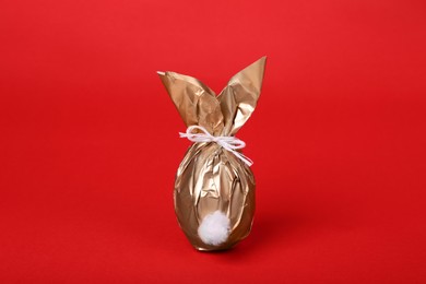Photo of Easter bunny made of shiny gold paper and egg on red background