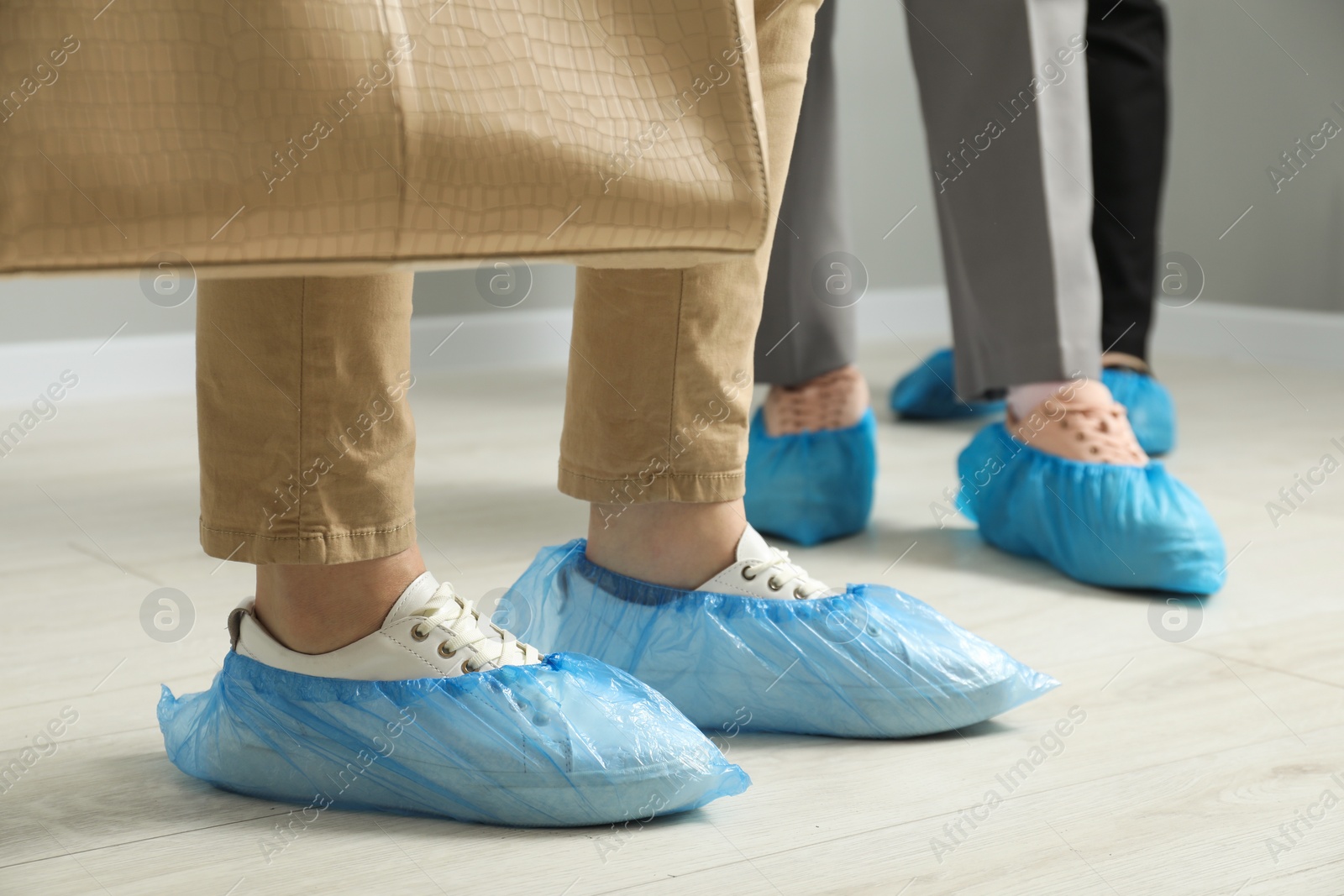 Photo of Women wearing blue shoe covers onto different footwear indoors, selective focus