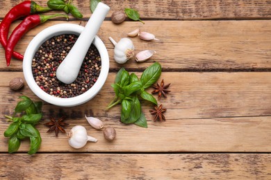 Photo of Mortar with pestle and different spices on wooden table, flat lay. Space for text