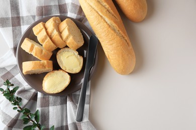 Photo of Whole and cut baguettes with fresh butter on table, flat lay