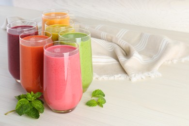 Colorful fruit smoothies and fresh mint on white wooden table. Space for text