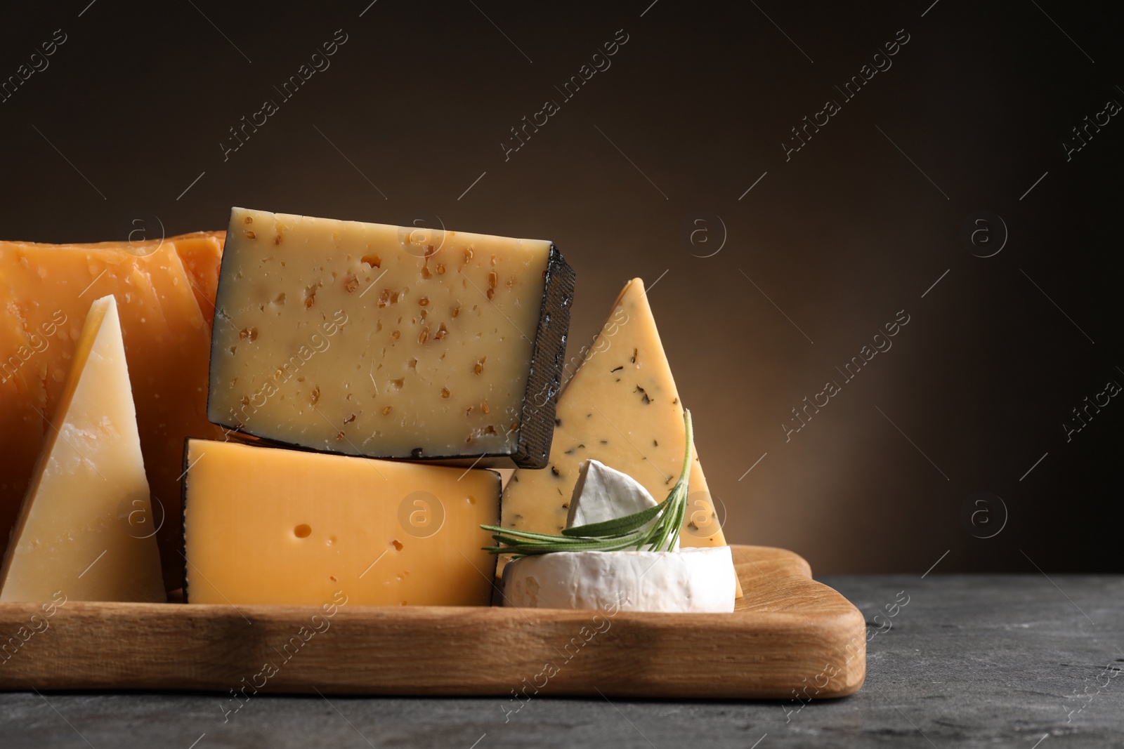 Photo of Wooden tray with different sorts of cheese and rosemary on grey table, space for text