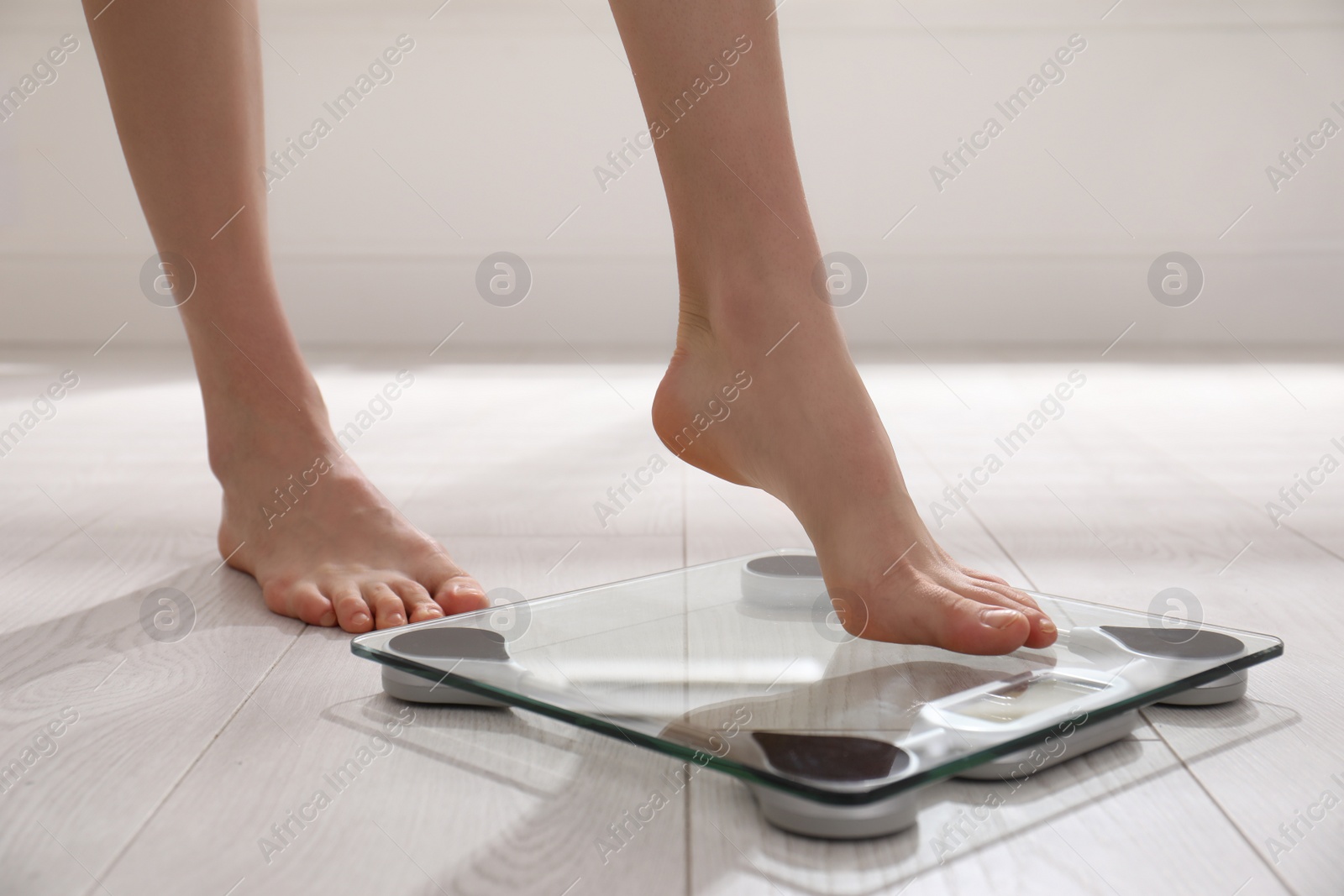 Photo of Woman stepping on floor scales indoors, closeup. Weight control