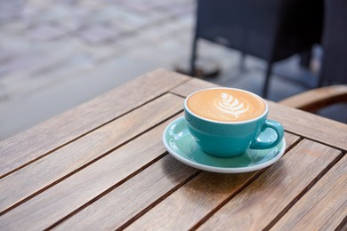 Cup of aromatic hot coffee on wooden table in outdoor cafe, space for text