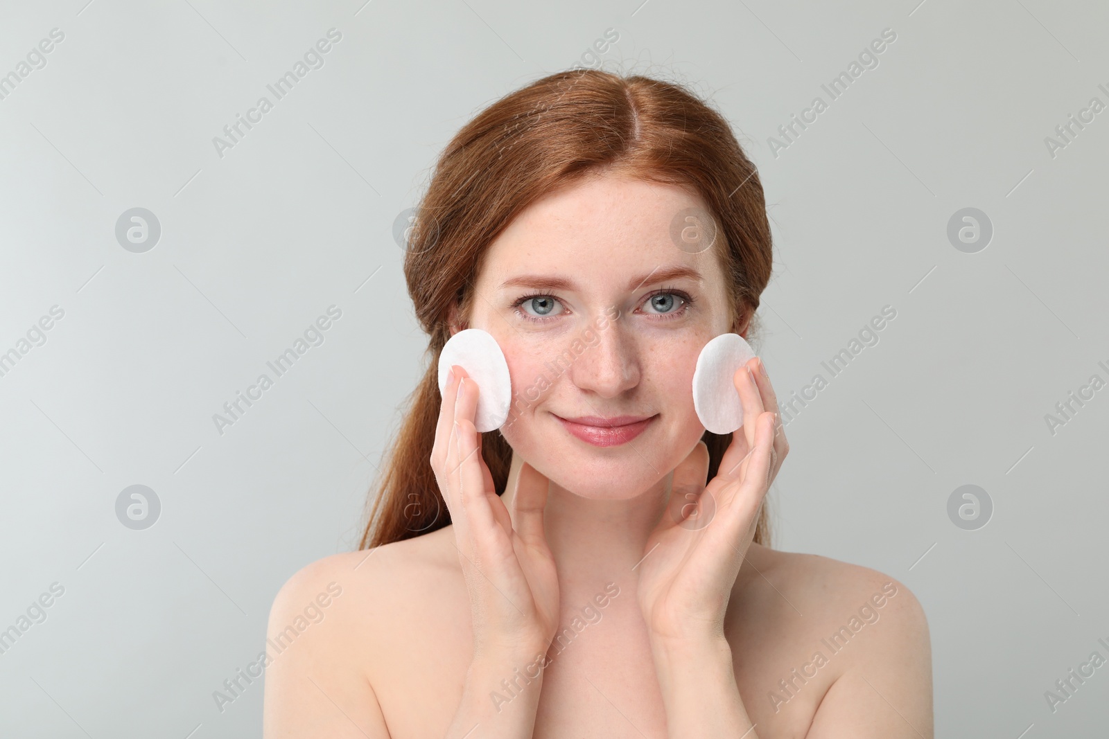 Photo of Beautiful woman with freckles wiping face on grey background