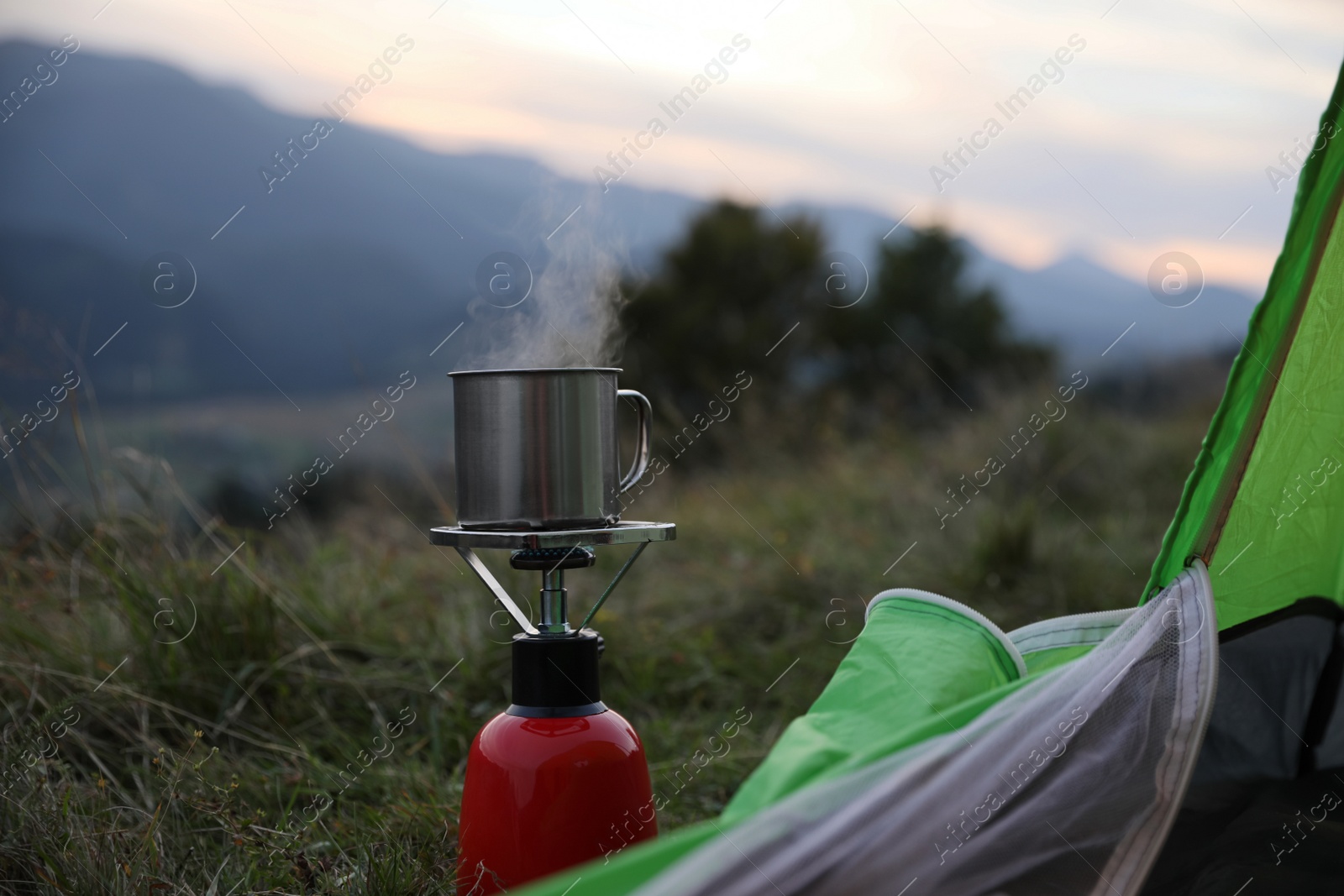 Photo of Boiling drink in metal mug on camping stove near tent outdoors