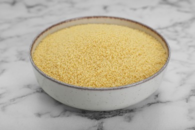 Photo of Bowl of raw couscous on white marble table, closeup