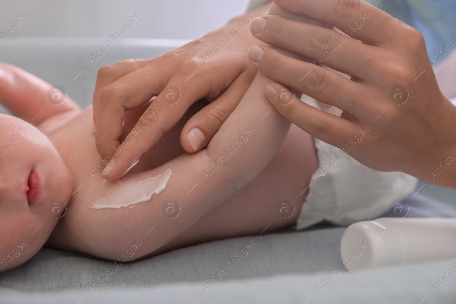 Photo of Mother applying moisturizing cream onto baby`s arm on changing table indoors, closeup