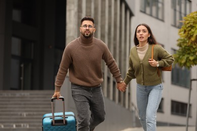Photo of Being late. Worried couple running near building outdoors