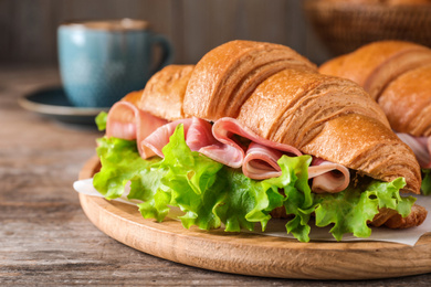 Photo of Tasty croissant sandwich with ham on wooden table, closeup