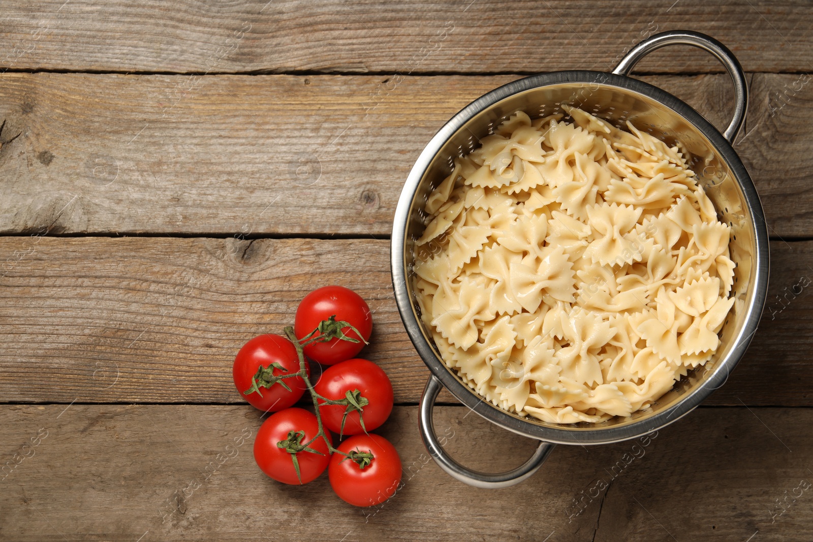 Photo of Cooked pasta in metal colander and tomatoes on wooden table, top view. Space for text