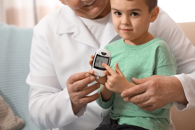 Doctor measuring patient's blood sugar level with digital glucose meter at home, closeup. Diabetes control