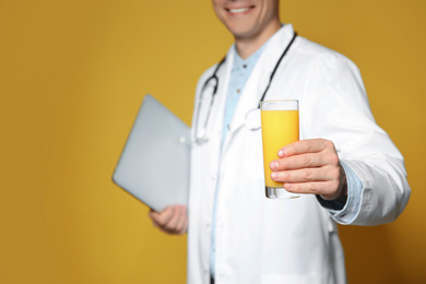 Nutritionist with glass of juice and laptop on yellow background, closeup
