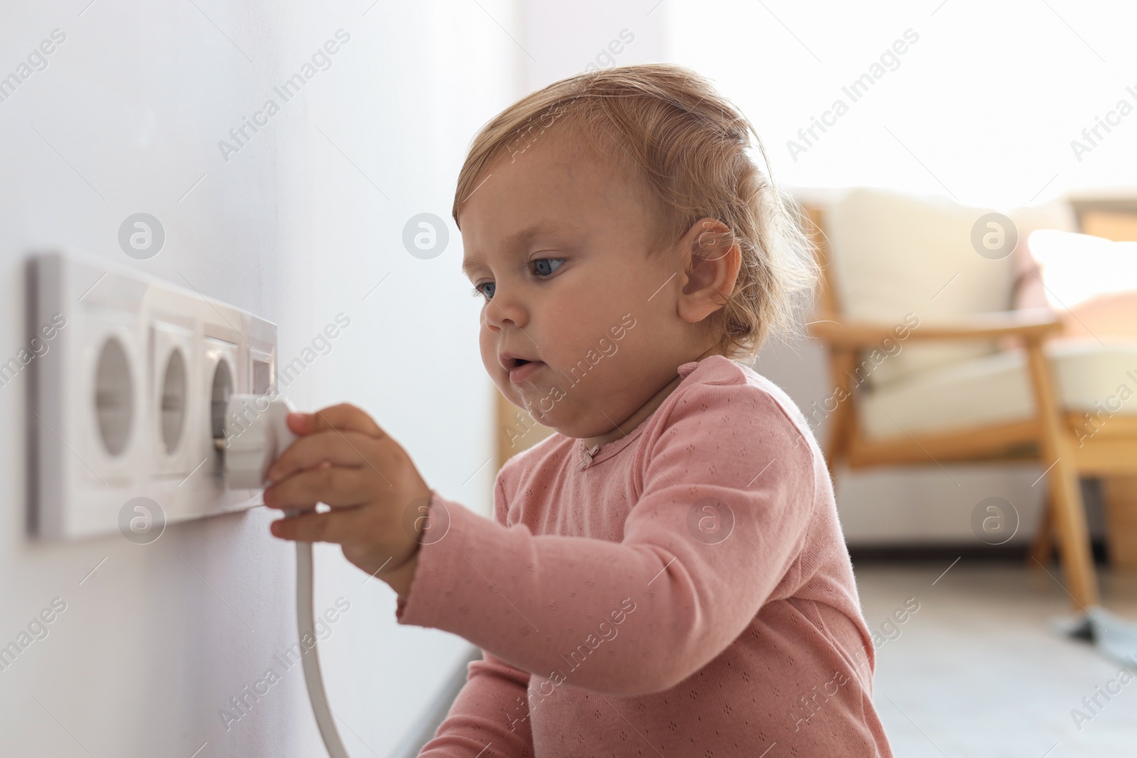 Photo of Cute baby playing with electrical socket and plug at home. Dangerous situation