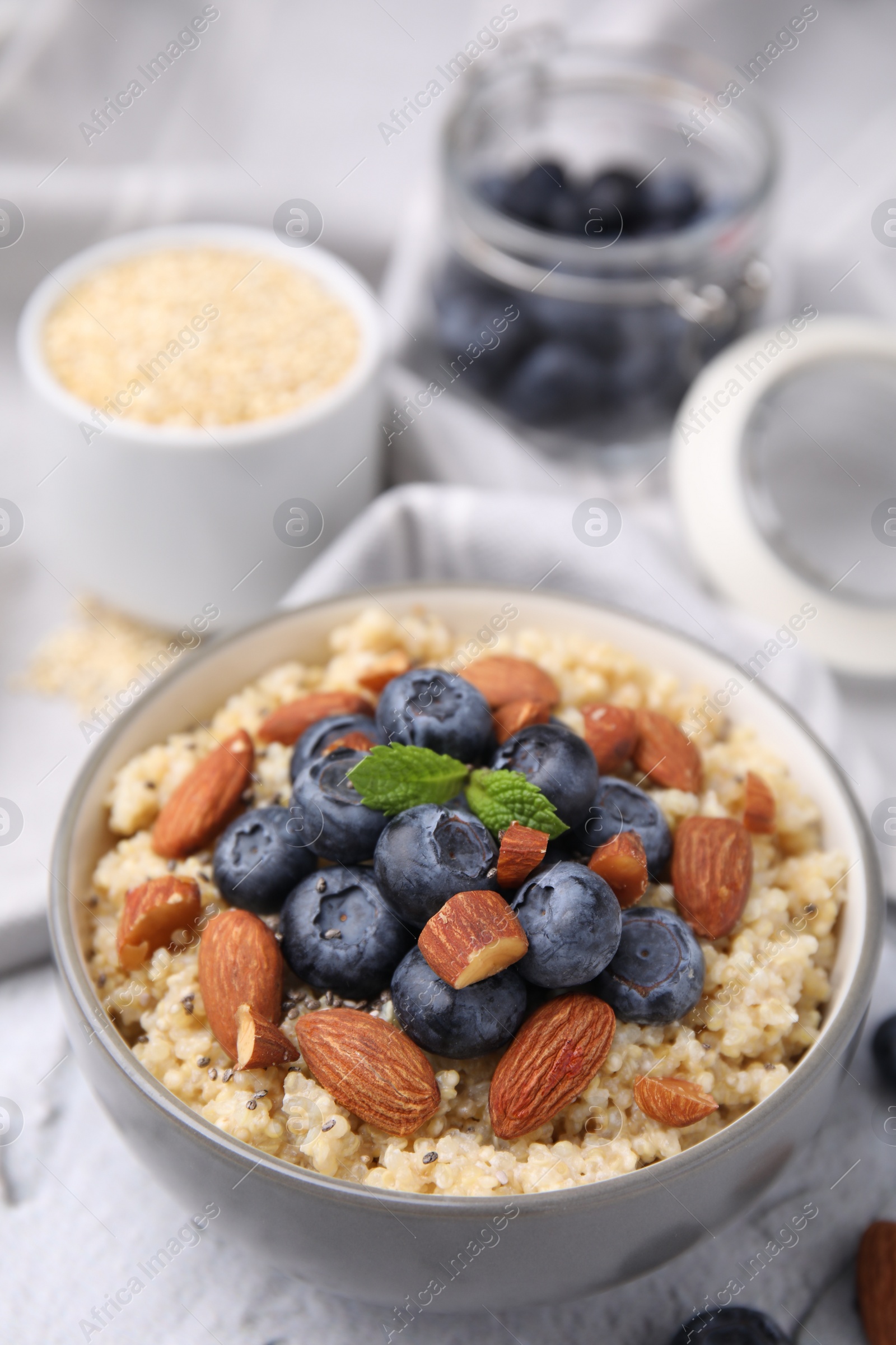 Photo of Bowl of delicious cooked quinoa with almonds and blueberries on white textured table, closeup