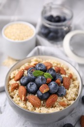 Bowl of delicious cooked quinoa with almonds and blueberries on white textured table, closeup