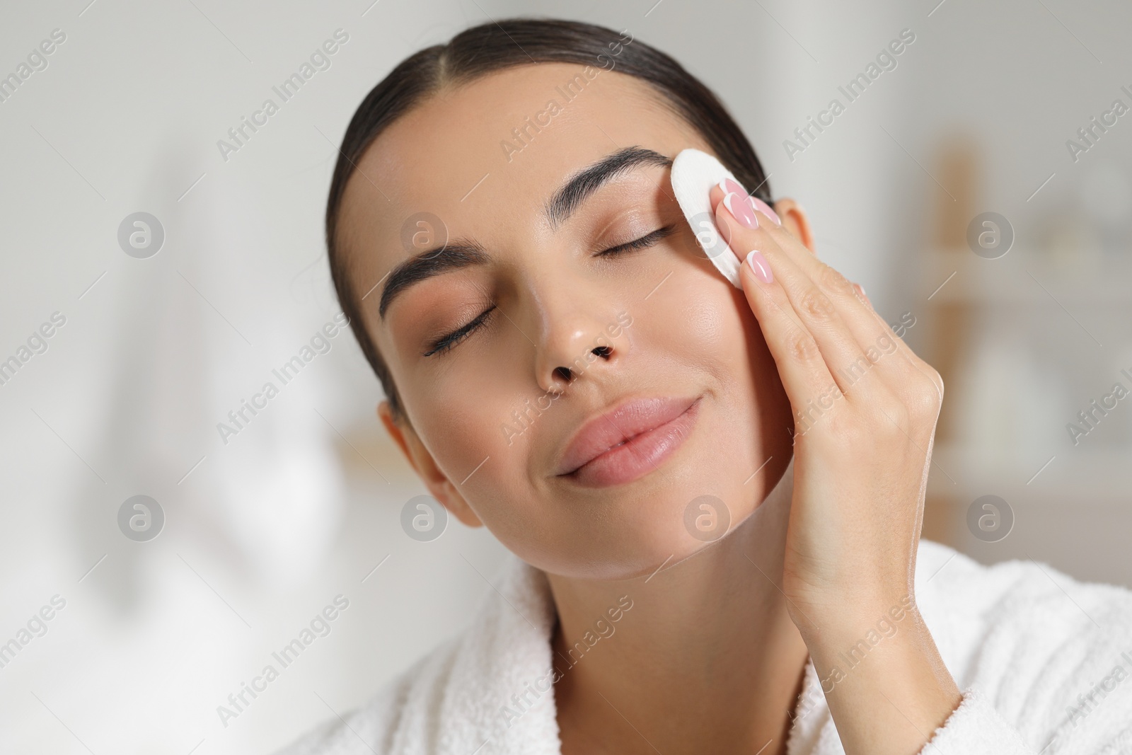 Photo of Beautiful woman removing makeup with cotton pad indoors