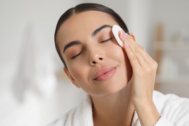 Beautiful woman removing makeup with cotton pad indoors