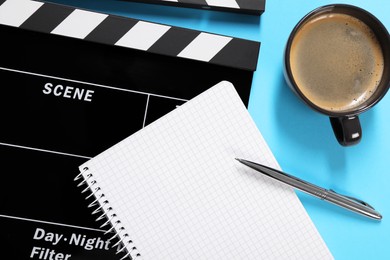 Movie clapper, coffee, notebook and pen on light blue background, flat lay