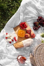 Photo of Picnic blanket with tasty food, flowers, basket and cider on green grass outdoors, flat lay