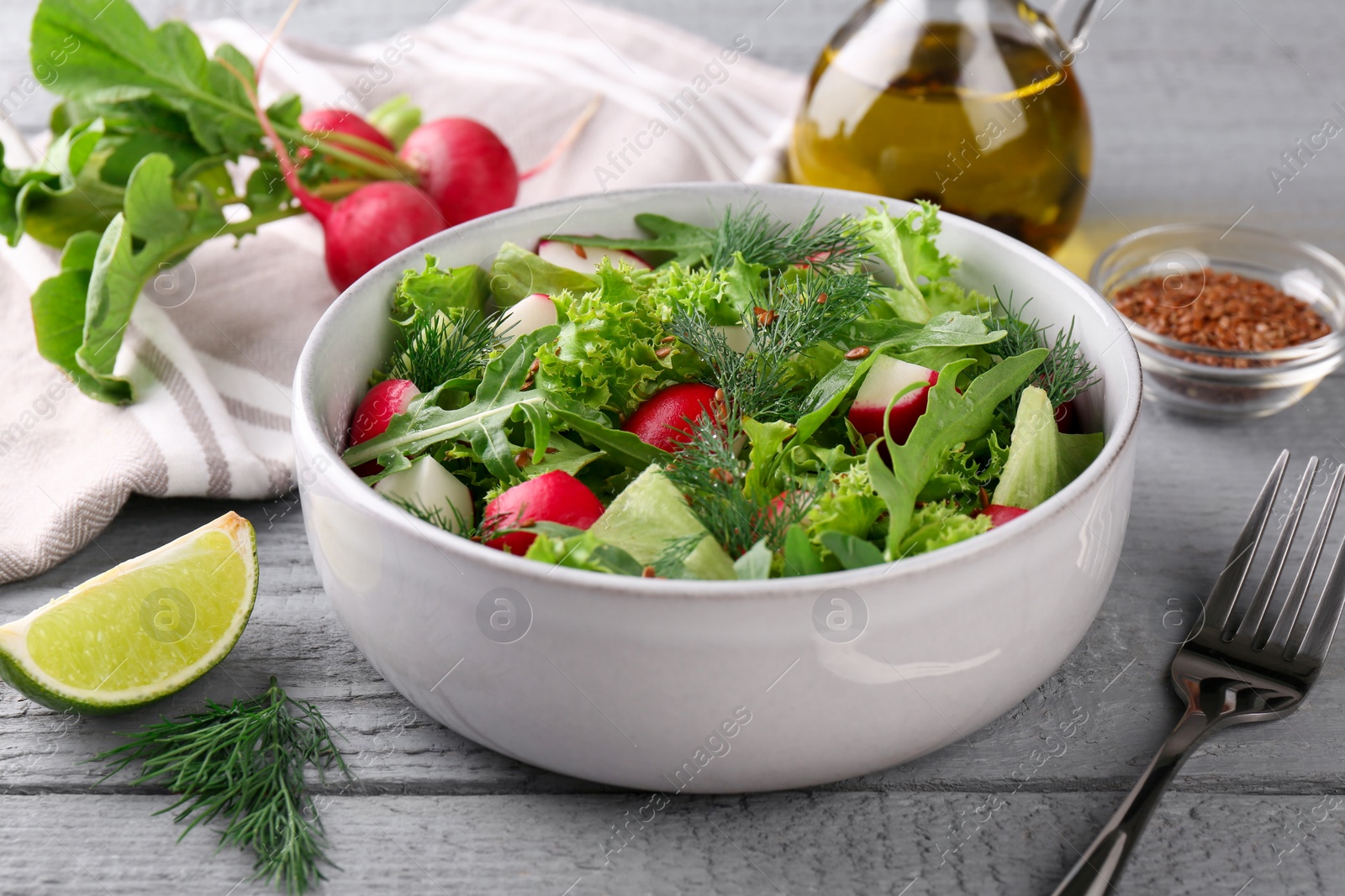 Photo of Delicious radish salad, ingredients and fork on light gray wooden table, closeup