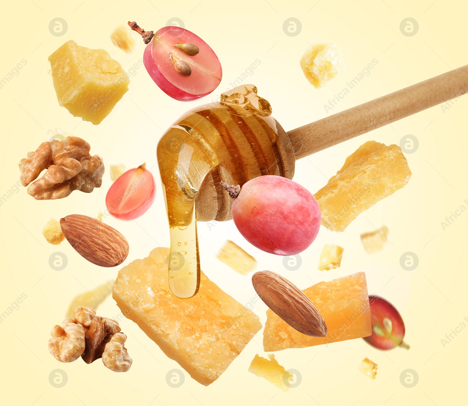 Image of Pieces of delicious parmesan, nuts, grapes and honey falling on yellow background