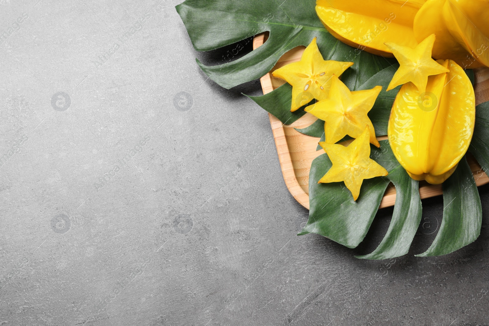 Photo of Delicious carambola fruits and green leaves on grey table, flat lay. Space for text