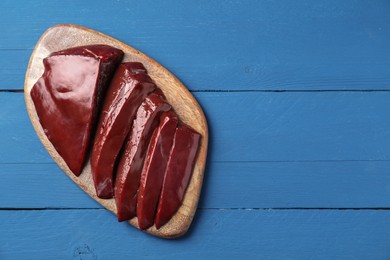 Photo of Cut raw beef liver on blue wooden table, top view. Space for text
