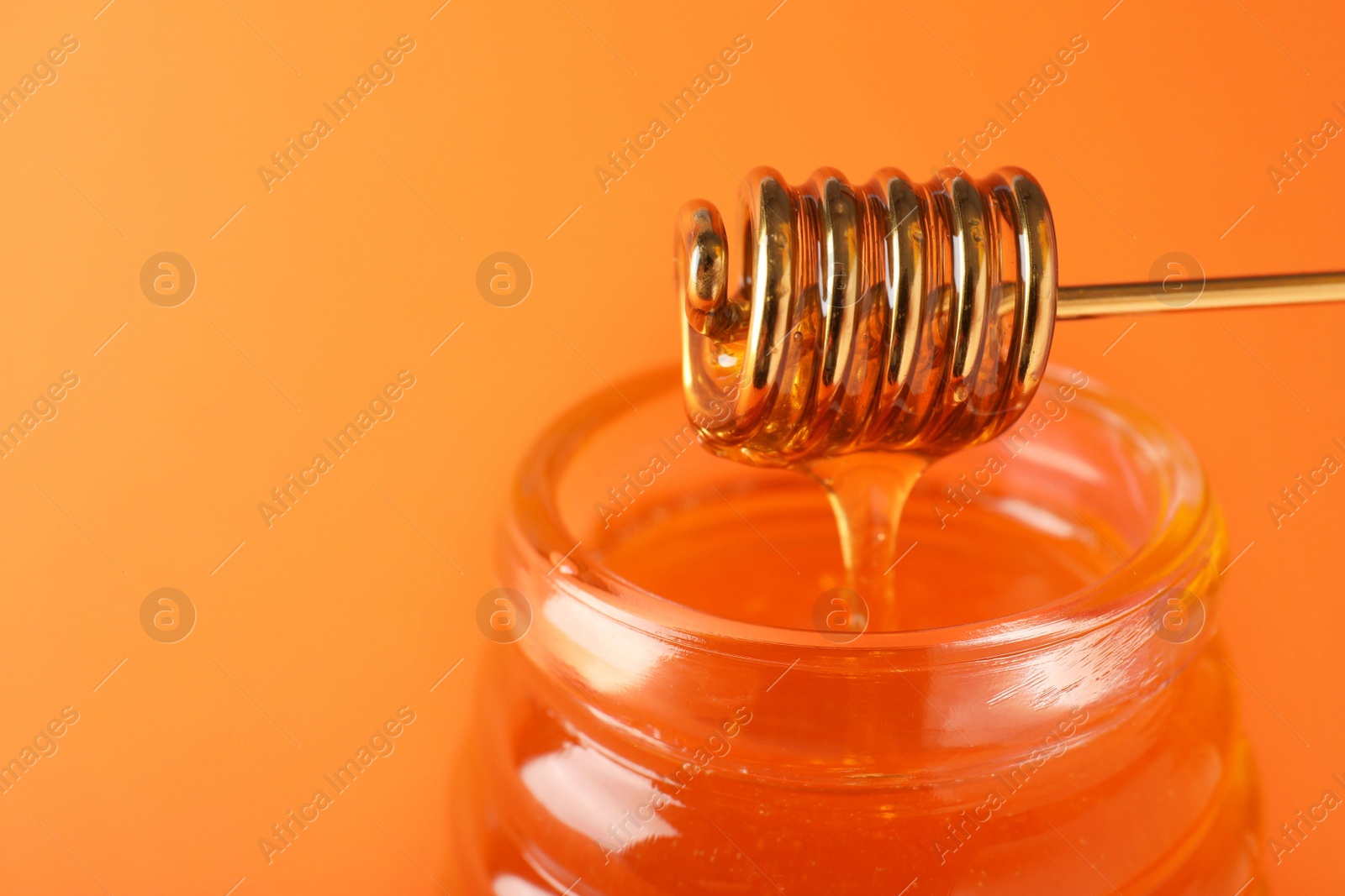 Photo of Jar of organic honey and dipper on orange background, closeup. Space for text