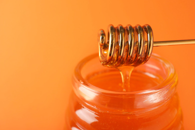 Photo of Jar of organic honey and dipper on orange background, closeup. Space for text