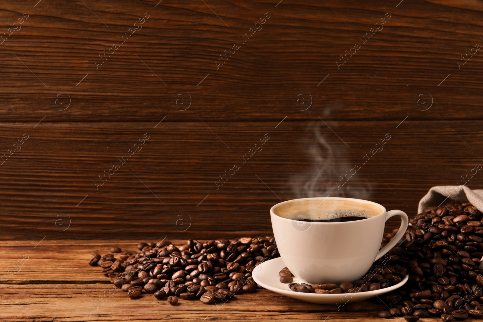 Image of Cup of aromatic hot coffee and beans on wooden table, space for text