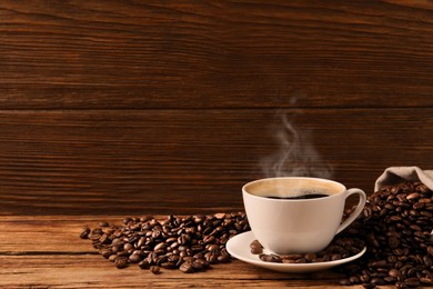 Image of Cup of aromatic hot coffee and beans on wooden table, space for text