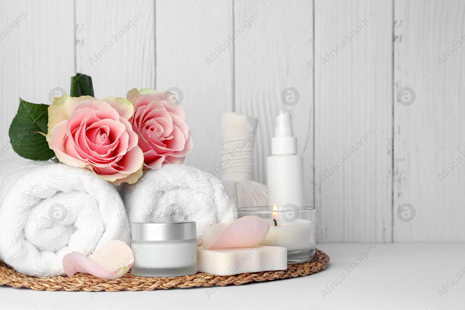 Photo of Composition with different spa products, roses and candle on white table against wooden background. Space for text